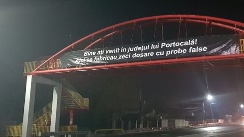 Banner pe DN 1 pe mesajul ”Bine ați venit în județul lui Portocală! Aici se fabricau zeci de dosare cu probe false”