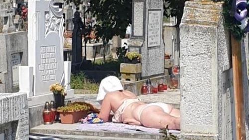 La plajă, într-un cimitir din Alba Iulia. O femeie și-a întins pătura pe un mormânt, sub razele soarelui